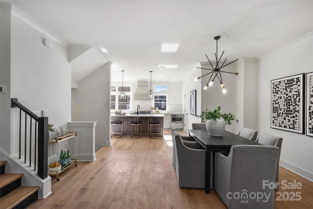 dining room featuring a notable chandelier, sink, ornamental molding, and light hardwood / wood-style floors