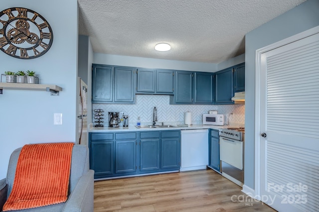 kitchen with sink, white appliances, backsplash, and blue cabinetry