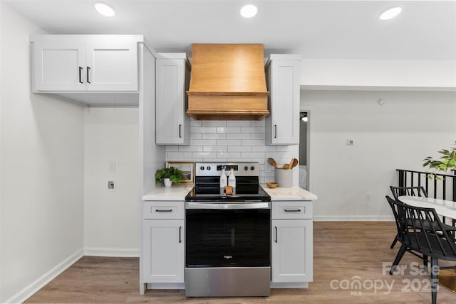 kitchen with stainless steel electric stove, white cabinets, premium range hood, backsplash, and light wood-type flooring