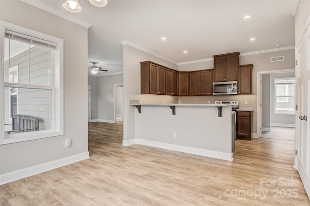 kitchen with range, a kitchen bar, ornamental molding, ceiling fan, and light hardwood / wood-style flooring