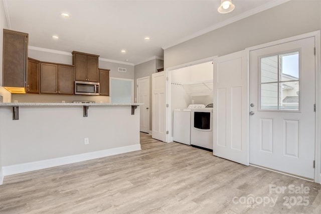 kitchen with washing machine and dryer, light hardwood / wood-style floors, a kitchen breakfast bar, kitchen peninsula, and crown molding