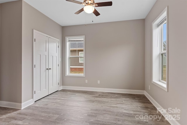 unfurnished bedroom with a closet, multiple windows, light wood-type flooring, and ceiling fan