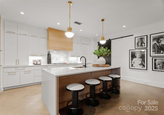 kitchen with decorative light fixtures, sink, white cabinetry, and a center island with sink