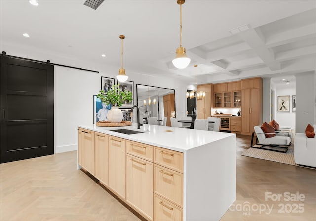 kitchen featuring decorative light fixtures, a barn door, sink, coffered ceiling, and a kitchen island with sink