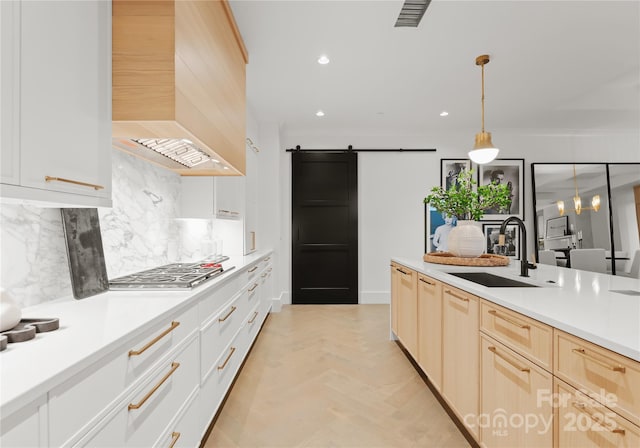 kitchen with custom exhaust hood, a barn door, decorative backsplash, hanging light fixtures, and sink