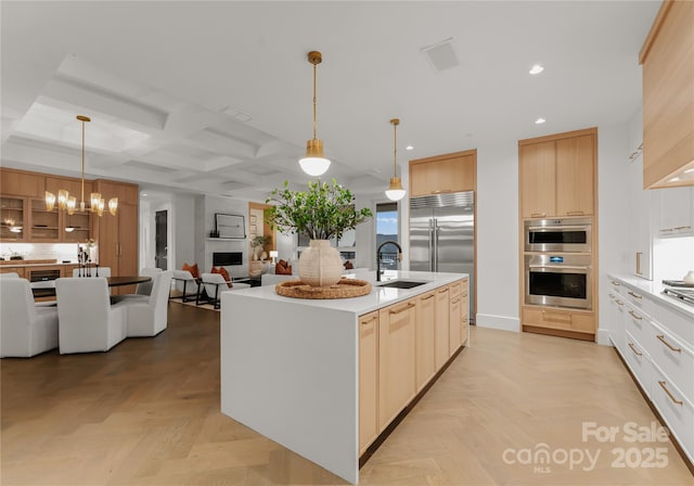 kitchen with light parquet floors, decorative light fixtures, coffered ceiling, and a kitchen island with sink