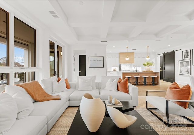 living room featuring beam ceiling, a barn door, sink, and coffered ceiling