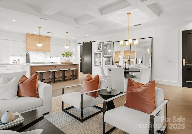 living room featuring a barn door, a notable chandelier, sink, beamed ceiling, and coffered ceiling