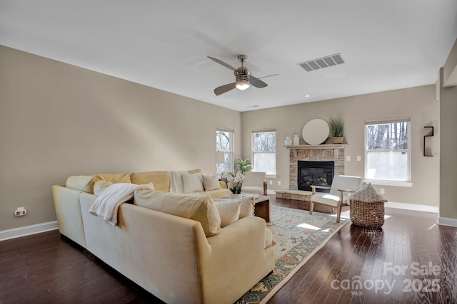 living room featuring ceiling fan, dark hardwood / wood-style flooring, and a stone fireplace