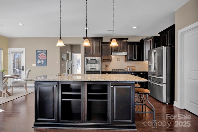 kitchen with appliances with stainless steel finishes, sink, hanging light fixtures, and an island with sink