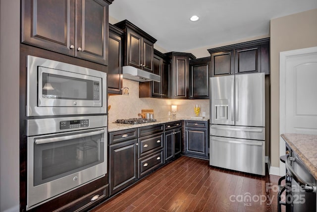 kitchen with tasteful backsplash, dark brown cabinets, light stone countertops, stainless steel appliances, and dark hardwood / wood-style flooring