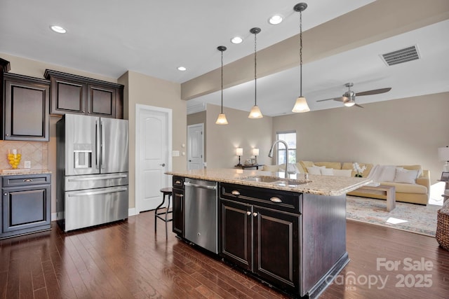 kitchen with decorative light fixtures, backsplash, a center island with sink, sink, and appliances with stainless steel finishes