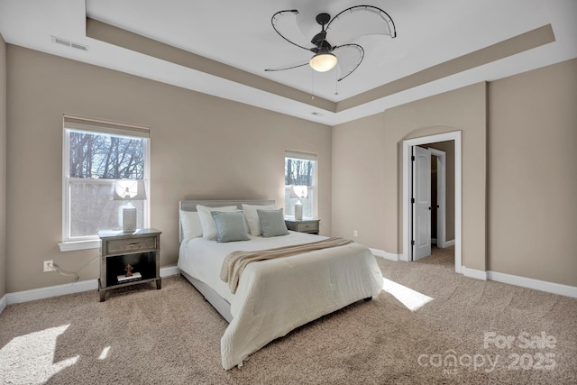 carpeted bedroom with a raised ceiling and ceiling fan