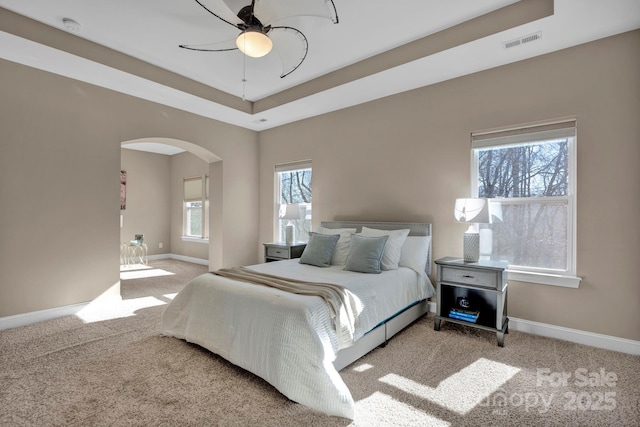 carpeted bedroom featuring ceiling fan and a tray ceiling