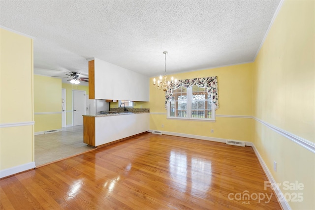 unfurnished dining area with ceiling fan with notable chandelier, sink, a textured ceiling, and light wood-type flooring