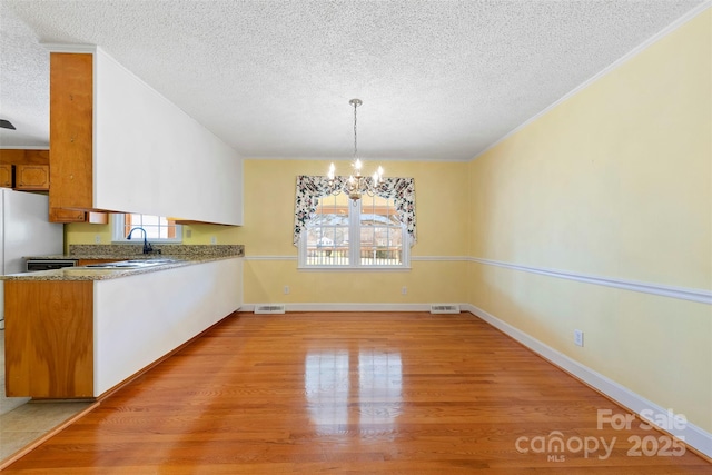 unfurnished dining area with sink, a textured ceiling, a notable chandelier, and light wood-type flooring