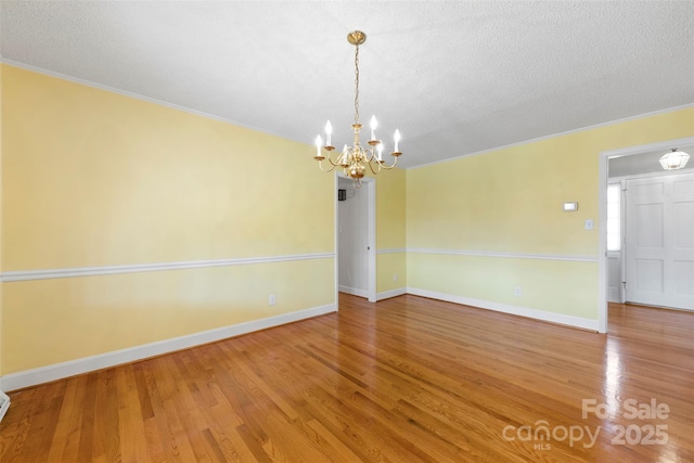 unfurnished room with ornamental molding, an inviting chandelier, a textured ceiling, and hardwood / wood-style floors