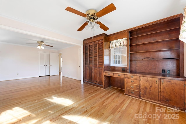 unfurnished office with built in desk, light wood-type flooring, ornamental molding, and ceiling fan