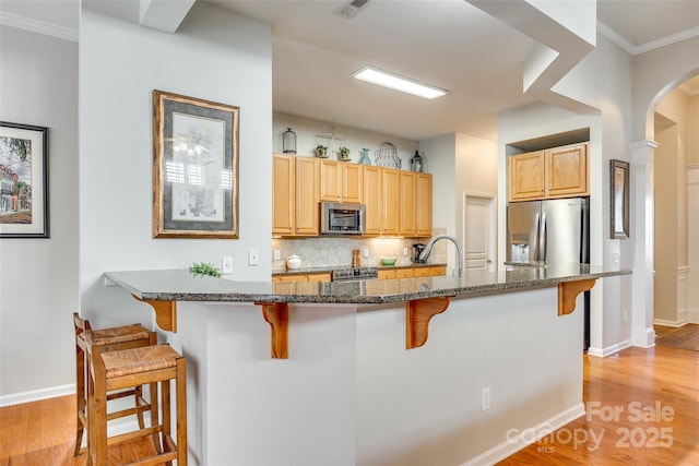 kitchen featuring light wood-type flooring, stainless steel appliances, dark stone countertops, and a breakfast bar