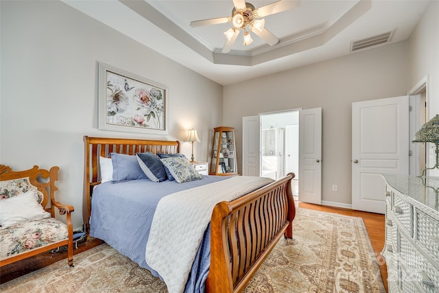 bedroom with light hardwood / wood-style floors, ceiling fan, connected bathroom, a tray ceiling, and crown molding