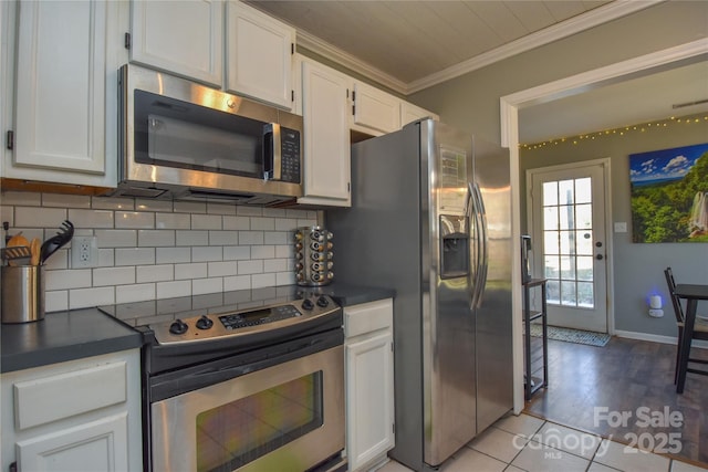 kitchen with light tile patterned floors, white cabinetry, appliances with stainless steel finishes, backsplash, and ornamental molding