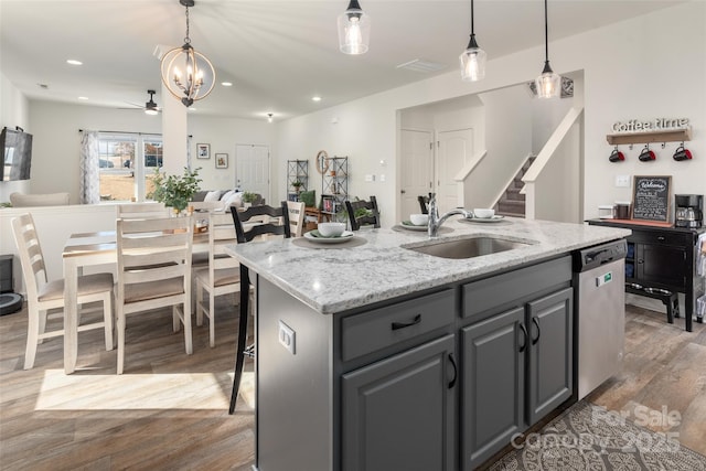 kitchen with decorative light fixtures, sink, a kitchen island with sink, stainless steel dishwasher, and light stone countertops