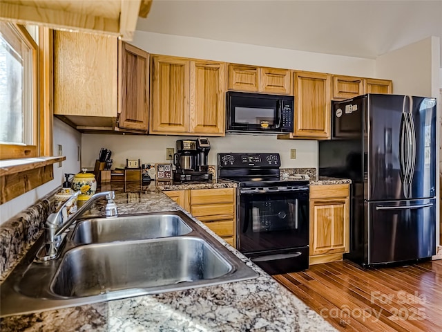 kitchen featuring dark stone countertops, dark hardwood / wood-style flooring, sink, and black appliances