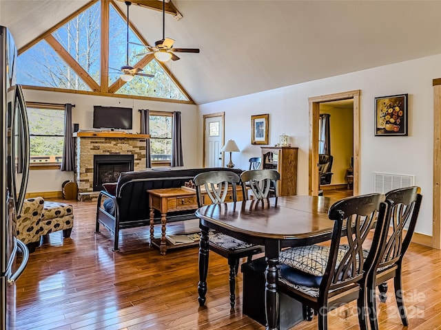 dining space with ceiling fan, a stone fireplace, hardwood / wood-style floors, and a wealth of natural light