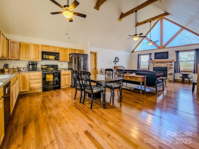 kitchen with beam ceiling, high vaulted ceiling, a fireplace, black appliances, and light wood-type flooring