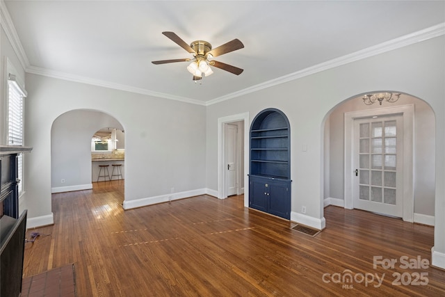 unfurnished living room with crown molding, dark wood-type flooring, built in shelves, and ceiling fan