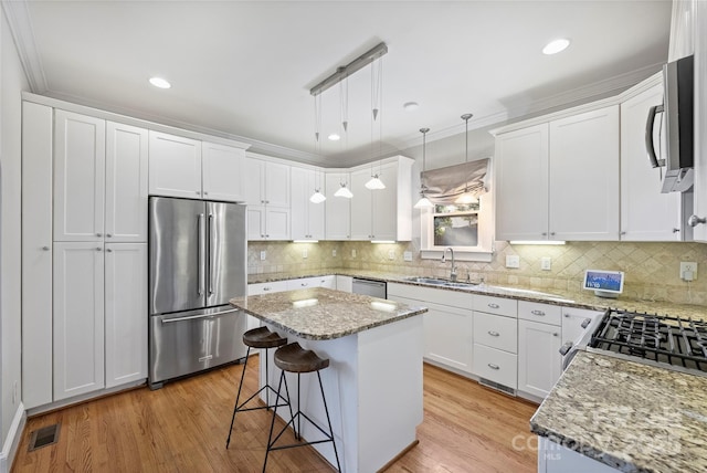 kitchen featuring sink, stainless steel appliances, white cabinets, a kitchen island, and decorative light fixtures