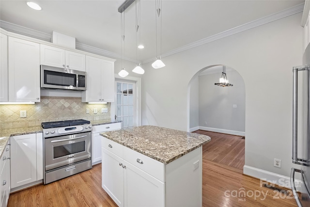 kitchen with a kitchen island, appliances with stainless steel finishes, decorative light fixtures, white cabinetry, and light stone countertops