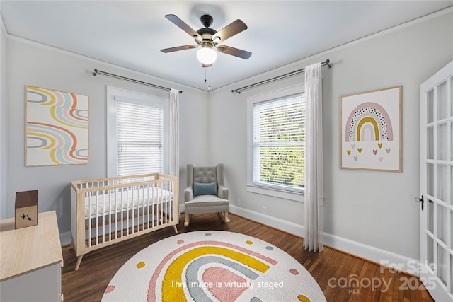 bedroom featuring a crib, dark wood-type flooring, and ceiling fan