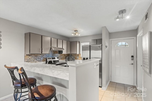 kitchen featuring light tile patterned flooring, appliances with stainless steel finishes, gray cabinetry, and kitchen peninsula