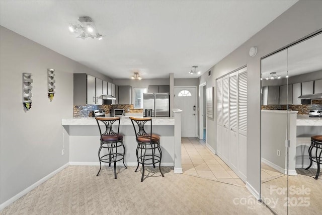 kitchen with kitchen peninsula, a breakfast bar, stainless steel refrigerator with ice dispenser, and gray cabinetry