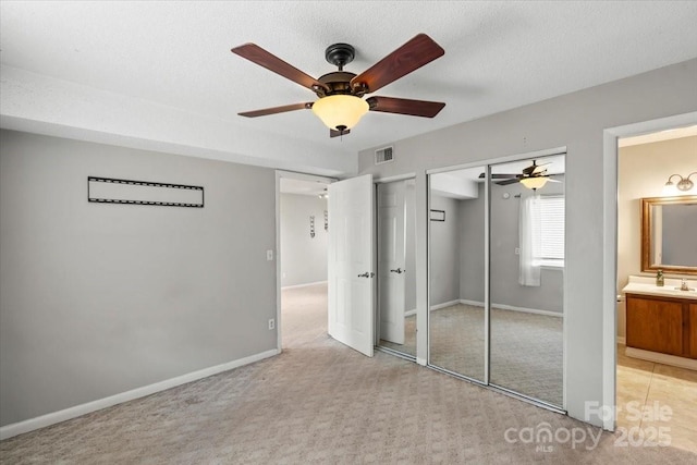 unfurnished bedroom with a textured ceiling, ensuite bath, sink, ceiling fan, and light colored carpet