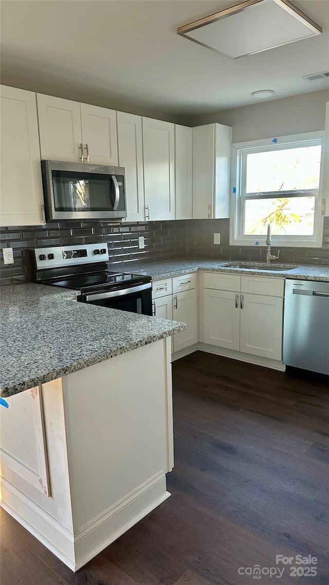 kitchen with white cabinets, appliances with stainless steel finishes, dark wood-type flooring, tasteful backsplash, and light stone counters