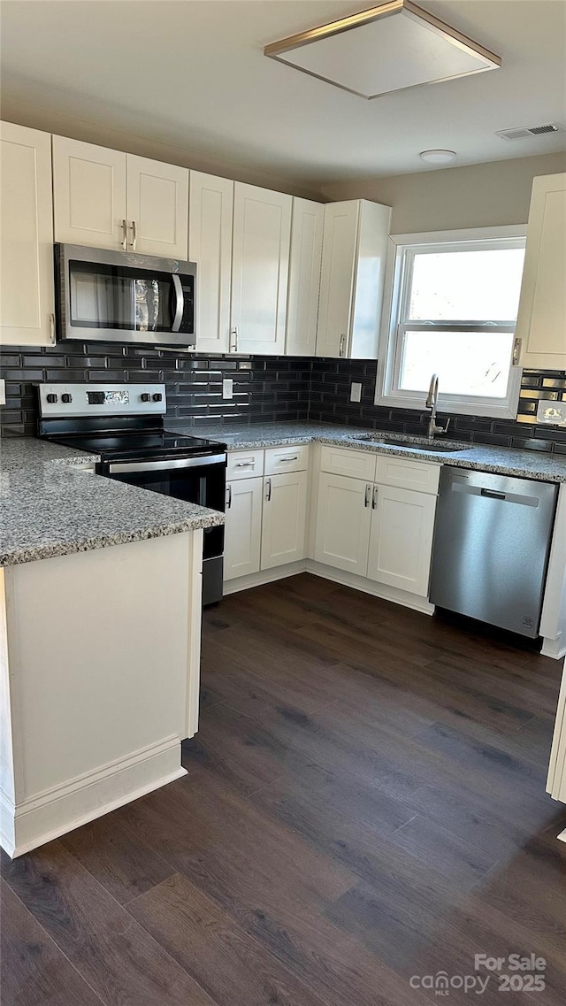 kitchen with white cabinetry, appliances with stainless steel finishes, dark hardwood / wood-style flooring, stone countertops, and sink