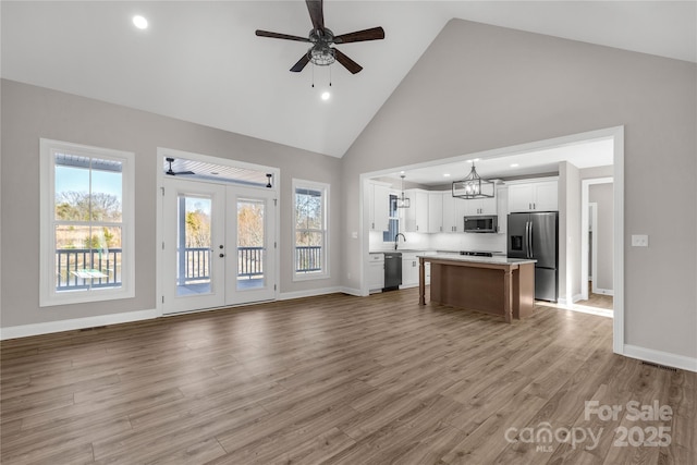 unfurnished living room featuring light wood-type flooring, ceiling fan with notable chandelier, french doors, and high vaulted ceiling