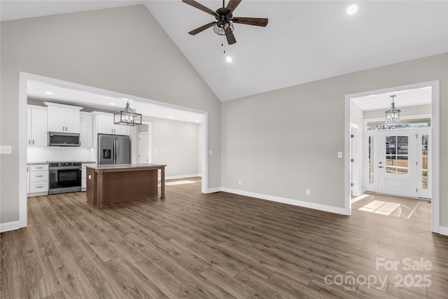 kitchen featuring a kitchen island, white cabinetry, hanging light fixtures, stainless steel appliances, and high vaulted ceiling