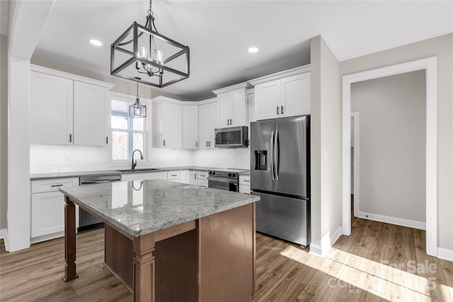 kitchen featuring white cabinets, appliances with stainless steel finishes, a kitchen island, sink, and light stone counters