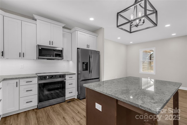 kitchen featuring pendant lighting, white cabinets, a center island, stainless steel appliances, and light hardwood / wood-style flooring