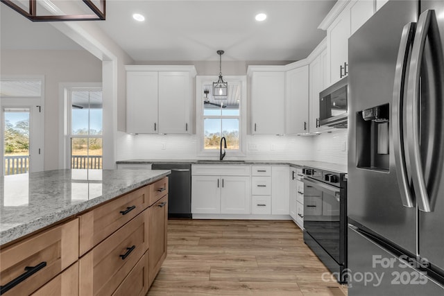 kitchen featuring appliances with stainless steel finishes, hanging light fixtures, light stone countertops, white cabinets, and sink