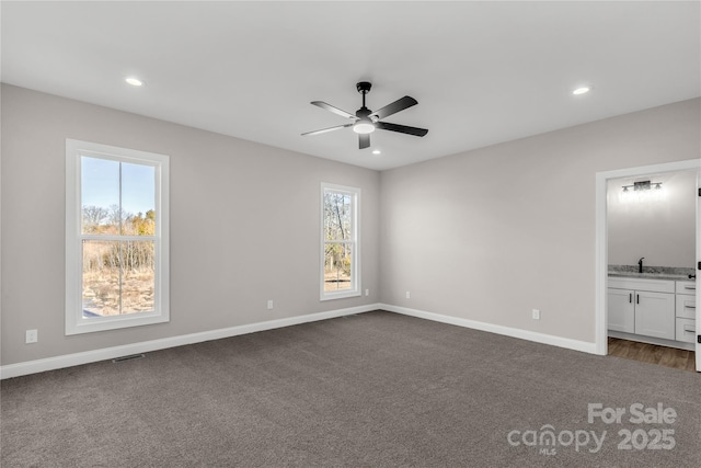 unfurnished bedroom with ceiling fan, connected bathroom, dark carpet, and multiple windows