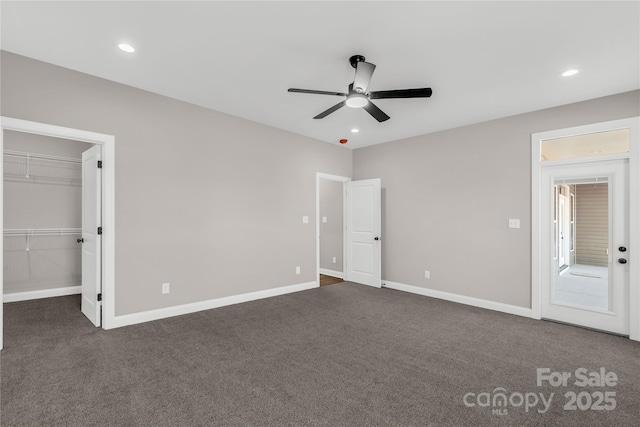 unfurnished bedroom with ceiling fan, a spacious closet, a closet, and dark colored carpet