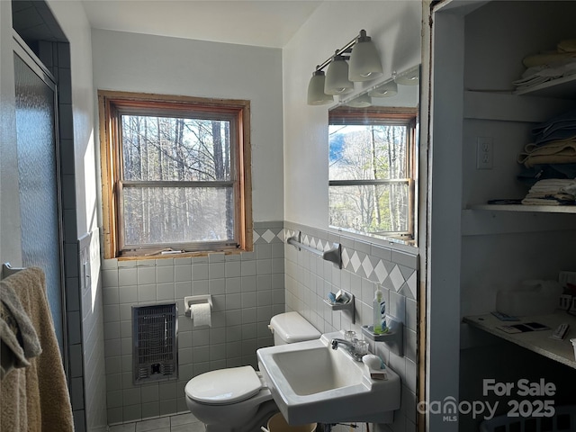 bathroom featuring tile patterned flooring, sink, tile walls, toilet, and heating unit