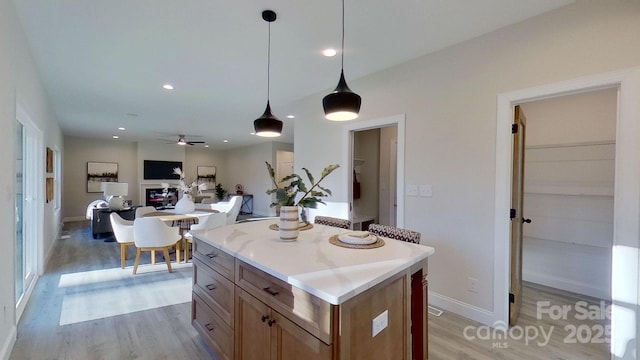 kitchen with hanging light fixtures, ceiling fan, a kitchen island, and light wood-type flooring