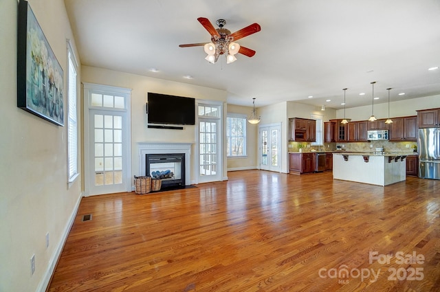 unfurnished living room with a fireplace with flush hearth, visible vents, plenty of natural light, and wood finished floors