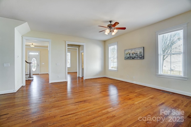 empty room with visible vents, stairway, light wood-style floors, ceiling fan, and baseboards