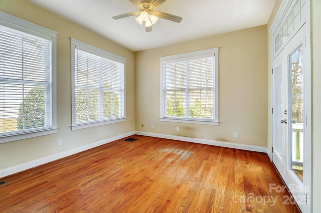 empty room with light wood finished floors, plenty of natural light, visible vents, and baseboards